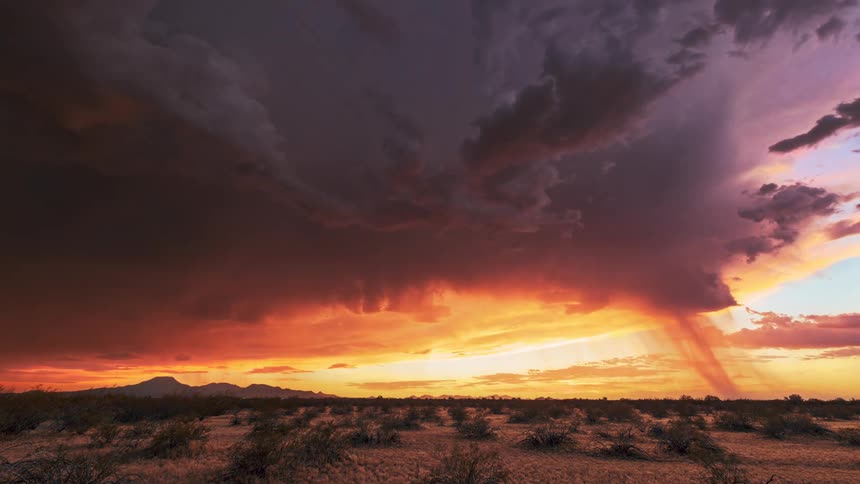 A stunning timelapse captures a massive storm cell unleashing a column of rain over the desert as the sky is set ablaze by a brilliant sunset