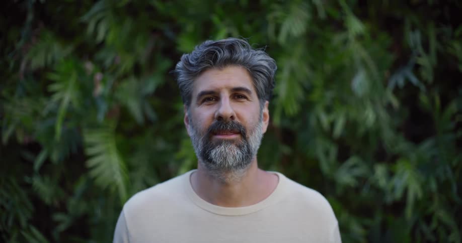Man smiles while standing outdoors near abundant vegetation on a summer day