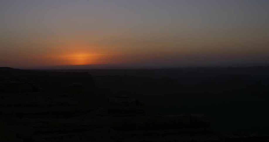 A vibrant orange sun slowly rises above a dark vast horizon casting a warm glow across the hazy morning sky the scene captures the transition from twilight to day as the suns golden light begins to illuminate the silhouette of the distant landscape