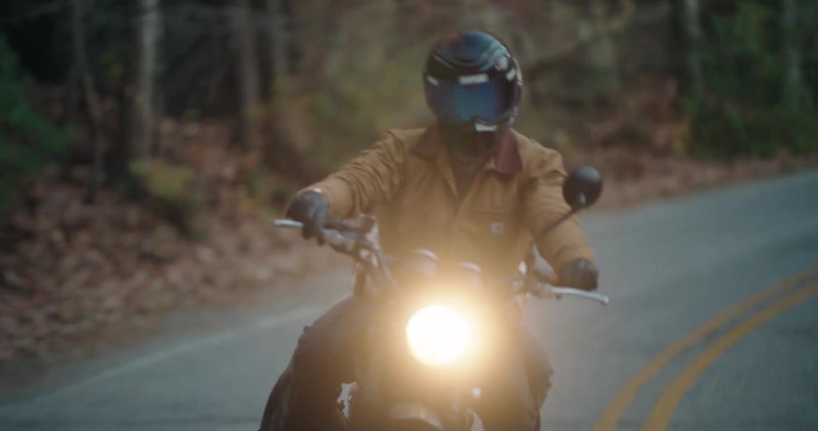 Two people on a motorcycle traveling along a highway surrounded by trees