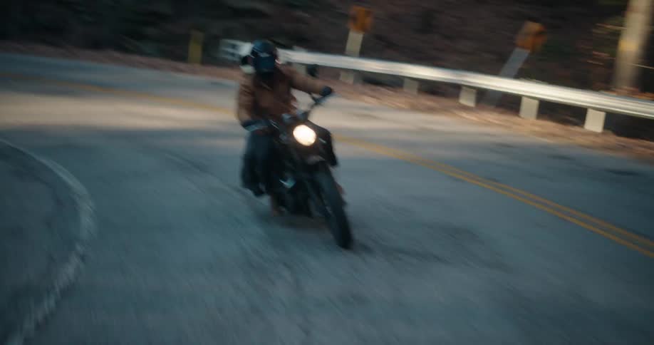 A motorcyclist with a passenger lean sharply into a curving forest road headlight glowing as motion blur and roadside guardrails emphasize speed and control