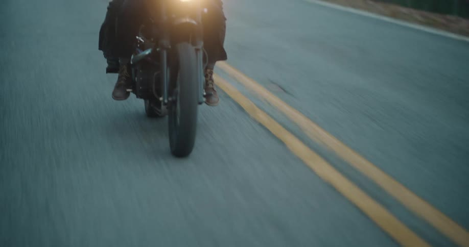 Headlight glows on a motorcycle traveling with a passenger on a road through the forest