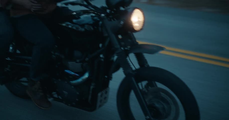 A man and a woman ride a black motorcycle along a paved road at dusk