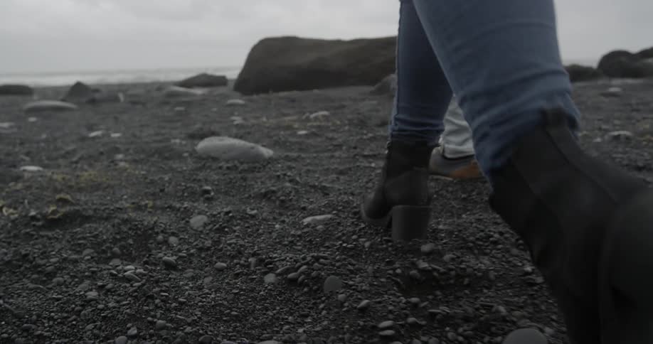 Two people walking on a rocky black beach