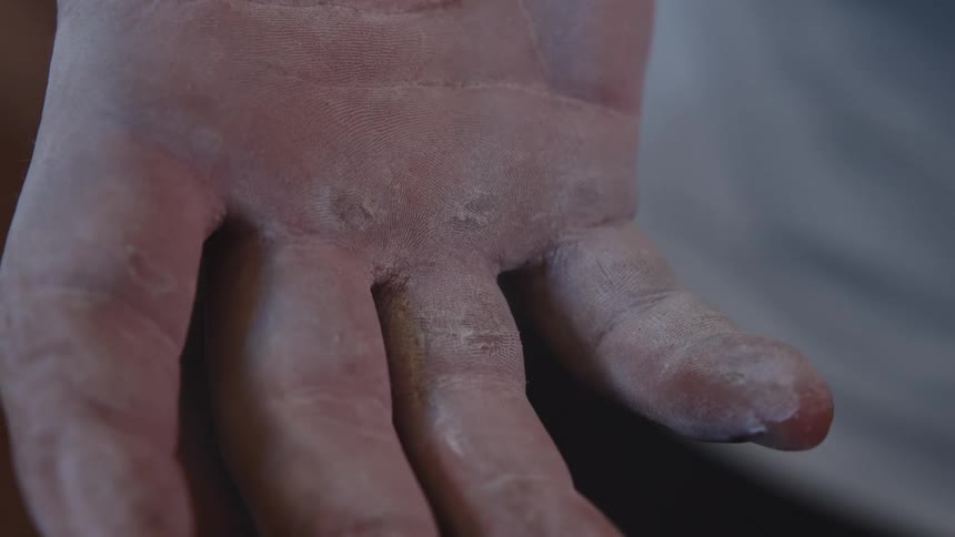 A closeup of an open human hand shows dry chalkdusted skin and roughened fingertips highlighting texture and wear against a softly blurred neutral background