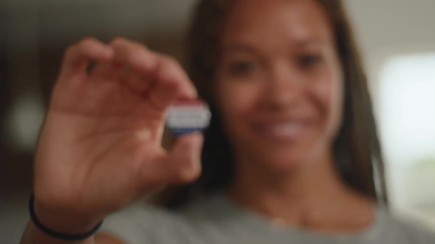 Person holds a pin reading i voted in an indoor setting with a blurred background