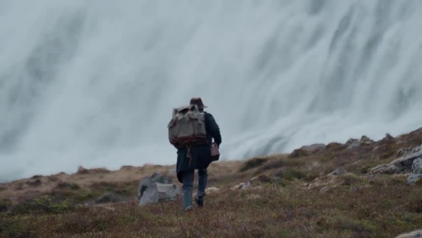 The man hikes towards the waterfall