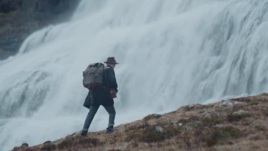 Person with a backpack hiking alongside a waterfall