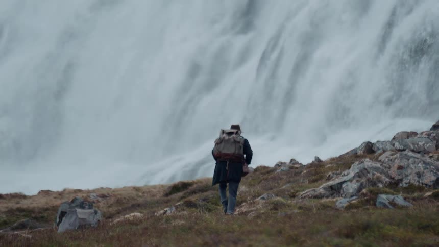 Adult man carrying a backpack walking near a waterfall outdoors