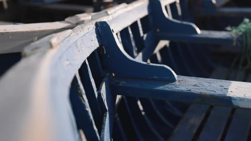 The footage captures a closeup shallowdepthoffield shot of the weathered blue wooden ribs and interior of a docked boat sunlight highlights the peeling paint and rustic texture of the timber as the camera gently pans across the structure