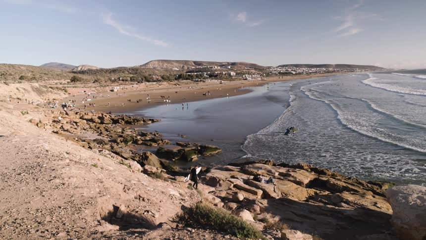 Wide beach with waves breaking along the shoreline people scattered on the sand and rocky formations in the foreground