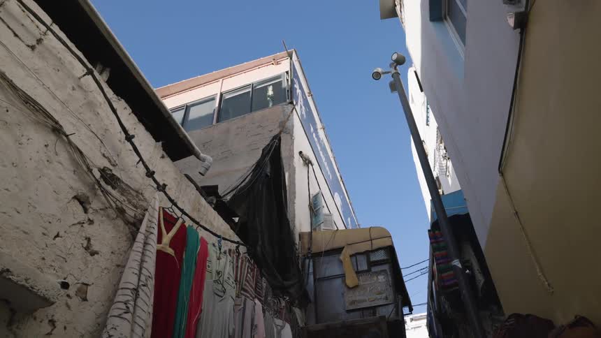 Narrow street between old buildings with clothes hanging on the walls and visible urban structures under a blue sky