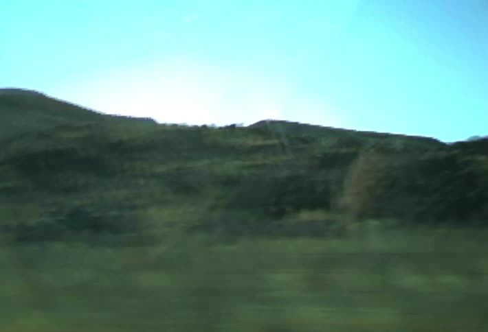 Vehicle drives past mountains and hills in the day during a road trip