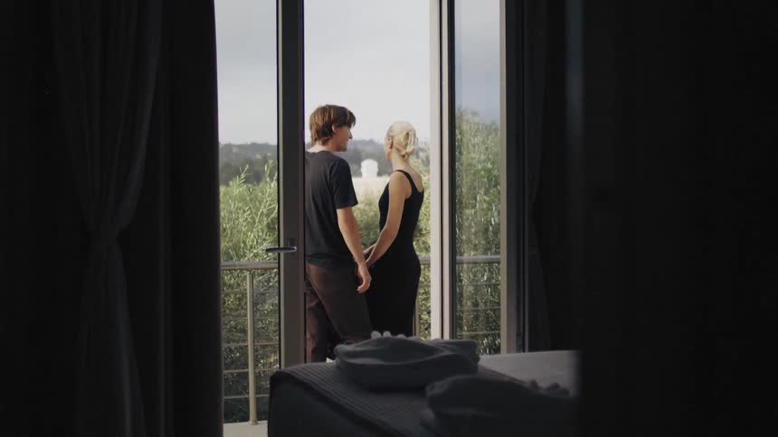 Two guests stand close together on the balcony of a hotel on a summer day