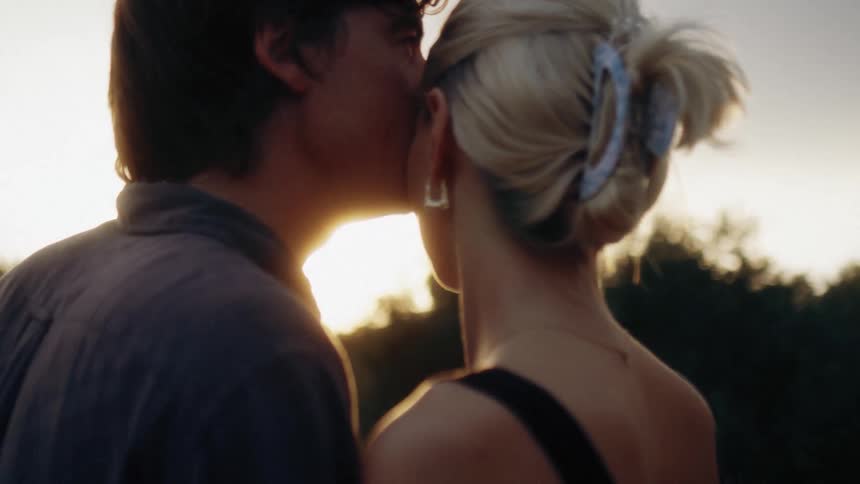 A young couple stands outdoors hugging each other as they watch the sunset