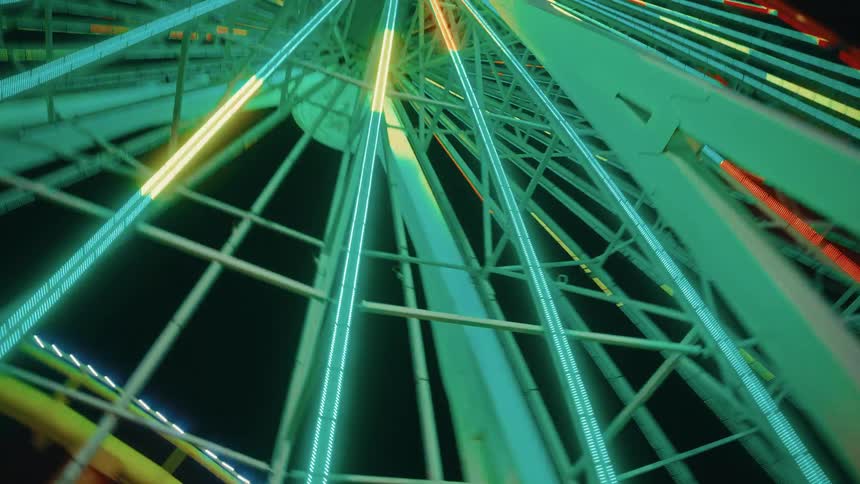 Glowing neon light strips trace the metal spokes of a towering ferris wheel at night forming a geometric pattern that converges toward the center against the dark sky