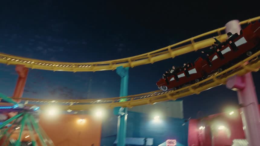 People ride on a roller coaster located next to a ferris wheel at night