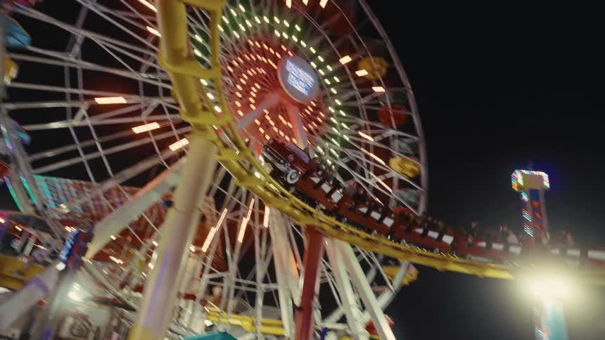 Person takes a video with her smartphone of people riding a rollercoaster at night