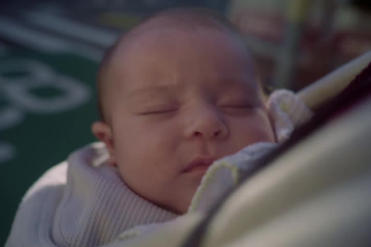 A newborn baby sleeps peacefully while being carried across a city street in a carrier