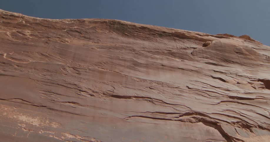 Slanted rock wall with visible sedimentary layers under a blue sky