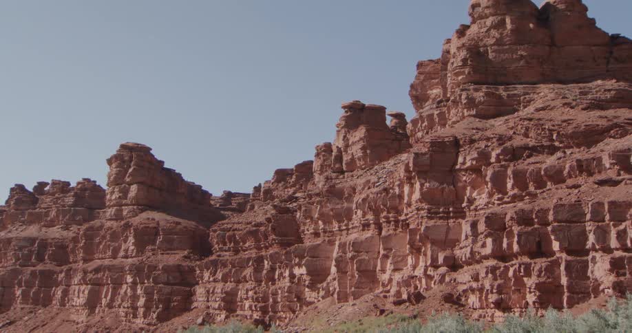 Sheer red sandstone cliffs rise above a calm river their layered faces catching the clear desert light