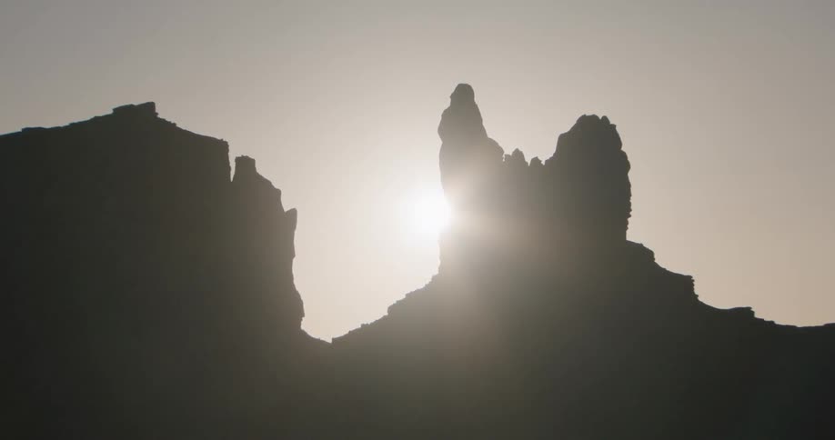 The sun peeks through a narrow gap between jagged rock silhouettes in a vast desert landscape