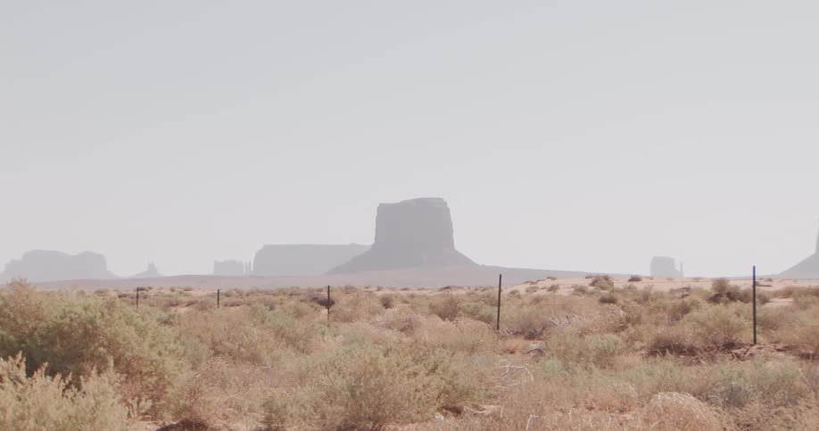 Sparse desert brush stretches toward distant flattopped mesas softened by heat haze under a pale open sky