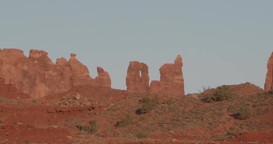 Red rock spires and towering buttes rise from a rugged desert plain under a clear blue sky