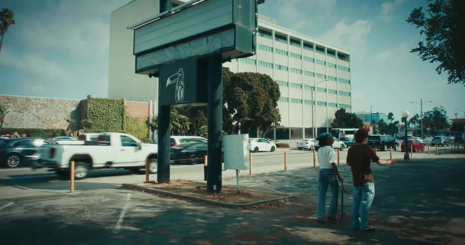 Pedestrians crossing an urban sidewalk beside a busy roadway with a commercial building in the background