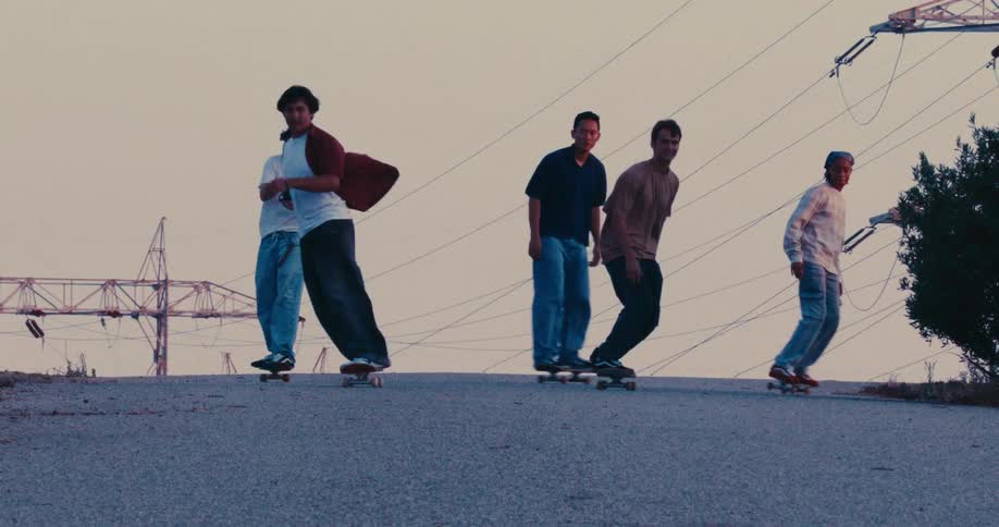 Group of young people walking and skateboarding on an urban street with overhead power lines in the background