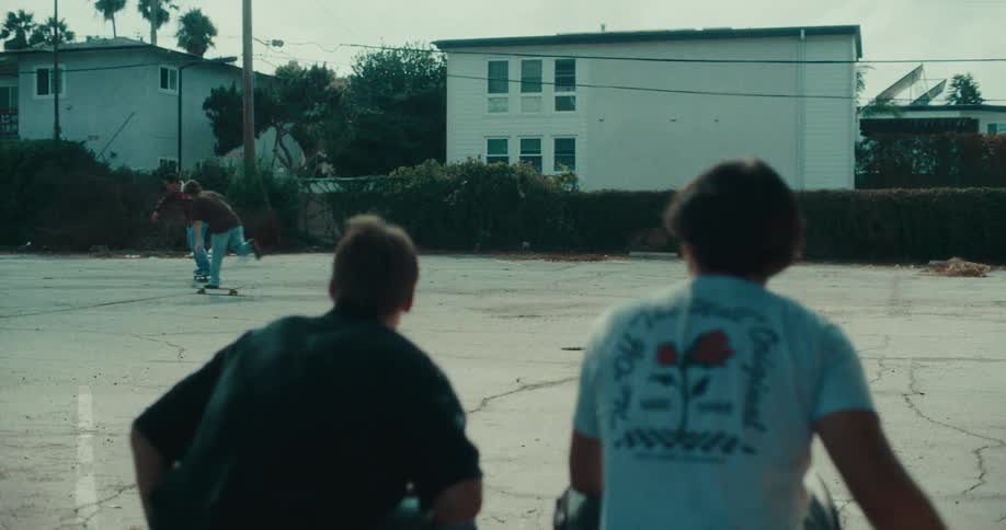 Teenagers skateboarding in an asphalt parking lot with a residential building in the background