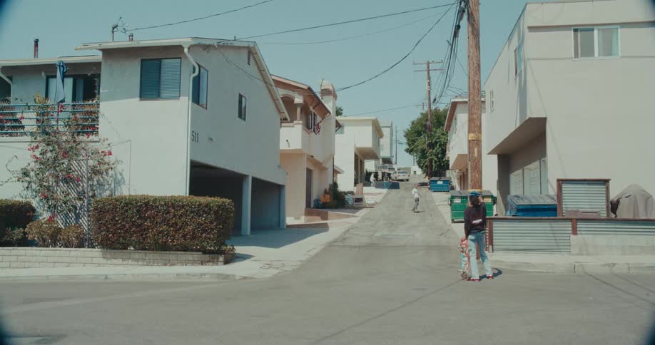 Young people with skateboards on a sloped residential street between houses and overhead wiring
