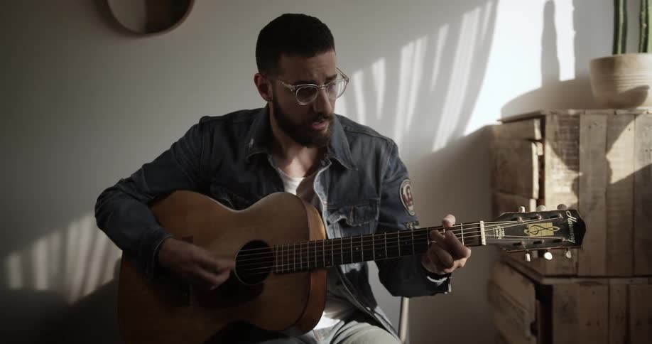 A man wearing glasses plays guitar