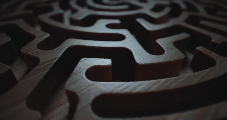 The camera moves in a lowangle tracking shot over the carved channels of a circular wooden labyrinth revealing the detailed grain and smooth texture of the timber as it travels toward the center of the dark intricate maze