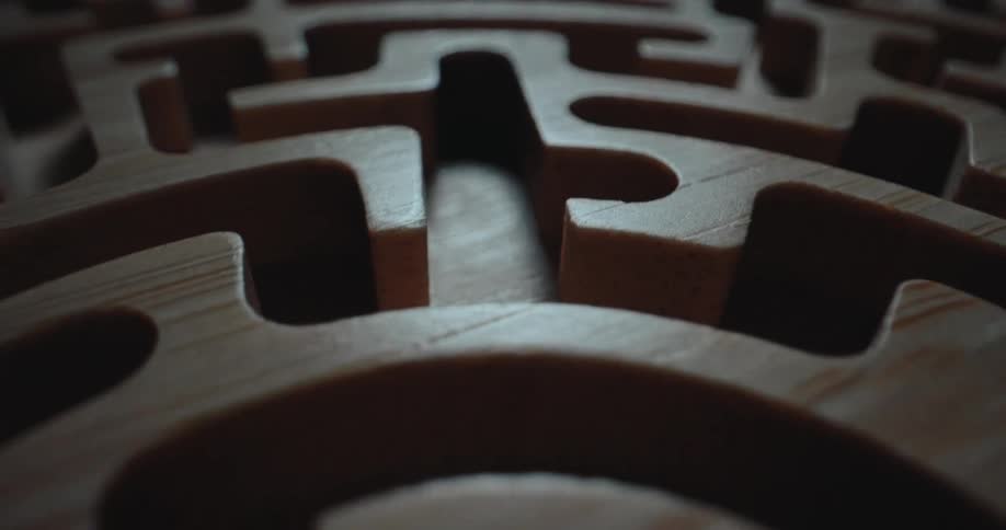 A classic wooden labyrinth maze game in a dark room with light reflecting off the wood