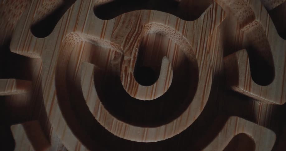 A topdown shot shows a circular wooden maze made of bamboo as it rotates slowly under a shifting light source