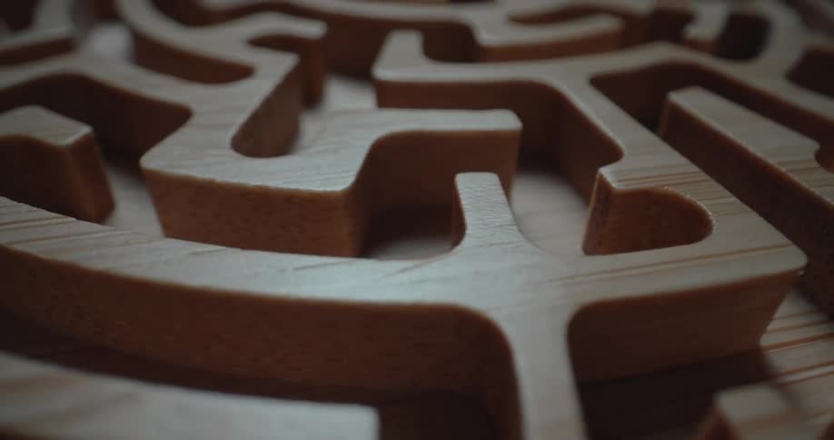 A classic wooden labyrinth maze game in a dark room with light reflecting off the wood