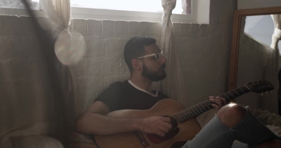A man leans against the wall playing guitar