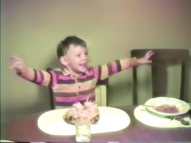 Boy eating dessert at the dinner table at home throws his arms out wide