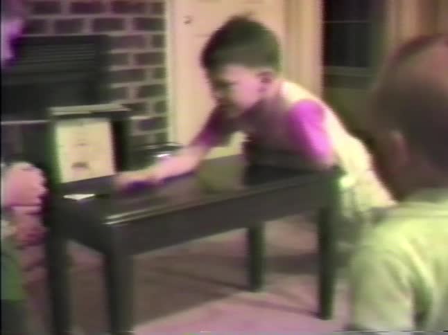 Toddler watches while boys play paper football in the living room