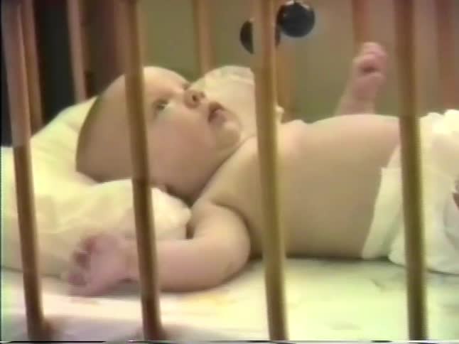 Baby lying in a crib with a light mattress and wooden rails