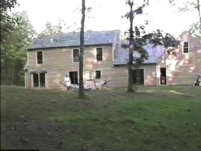 Adult standing outside of the house as a child swings in the hammock