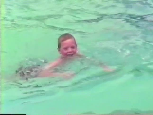 Little boy runs on a diving board and jumps into a neighborhood swimming pool with other boys and climbs out on the ladder