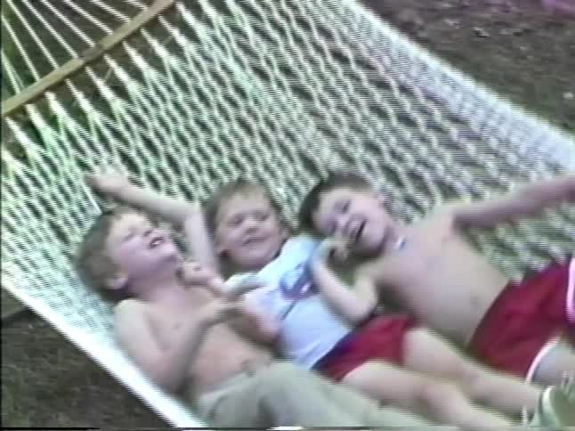 Three young boys happily swinging in a large hammock outdoors