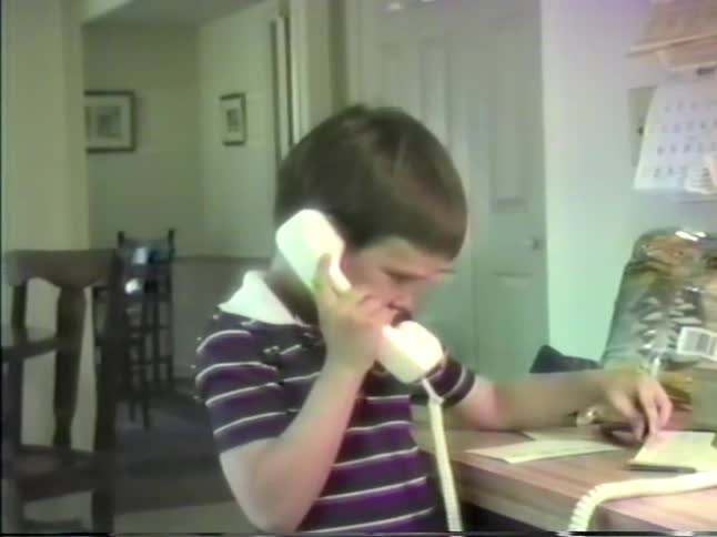 A boy is on the phone and then hands the phone to the person holding the camera