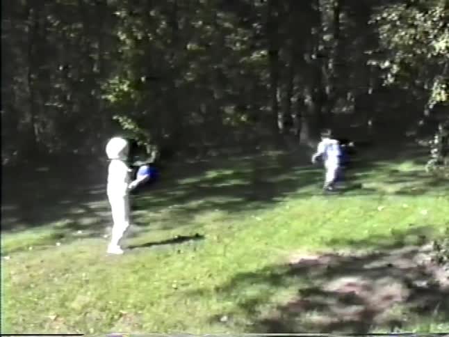 Two boys playing football in a yard as one boy catches the football and runs to the woods