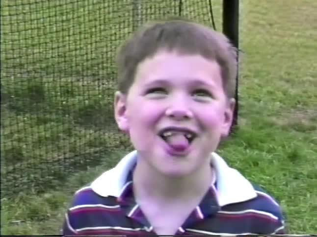 Child holding a can in a grassy area with a fence and another child in the background