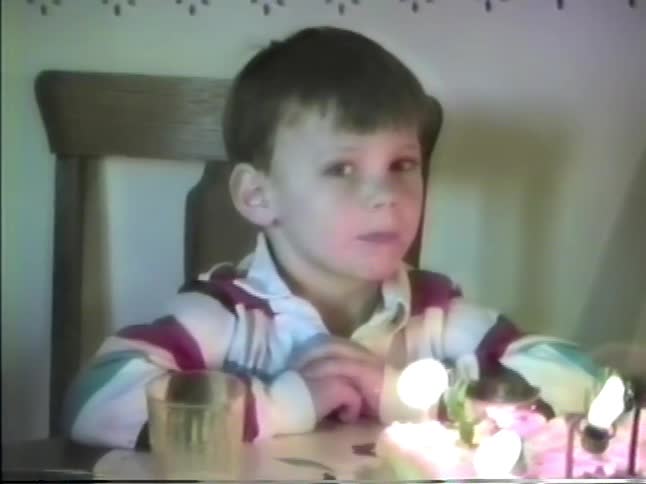 Boy takes multiple breaths to out the candles on his birthday cake during a party at home