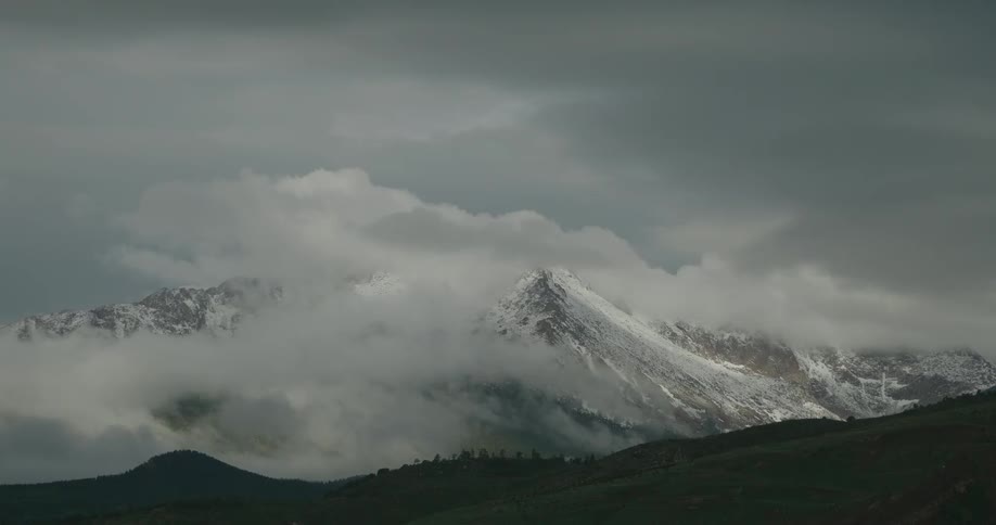 Mountain peaks with partial snow cover surrounded by clouds under an overcast sky