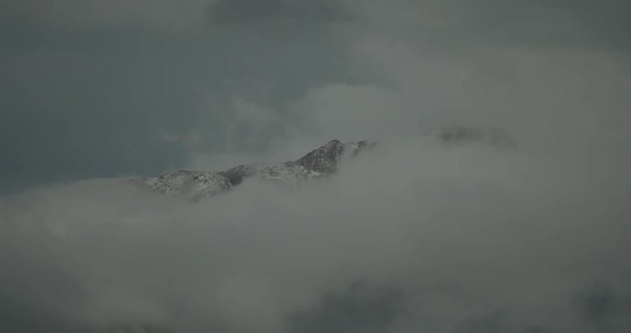 A mountain peak at midday covered in snow and surrounded by a foggy atmosphere